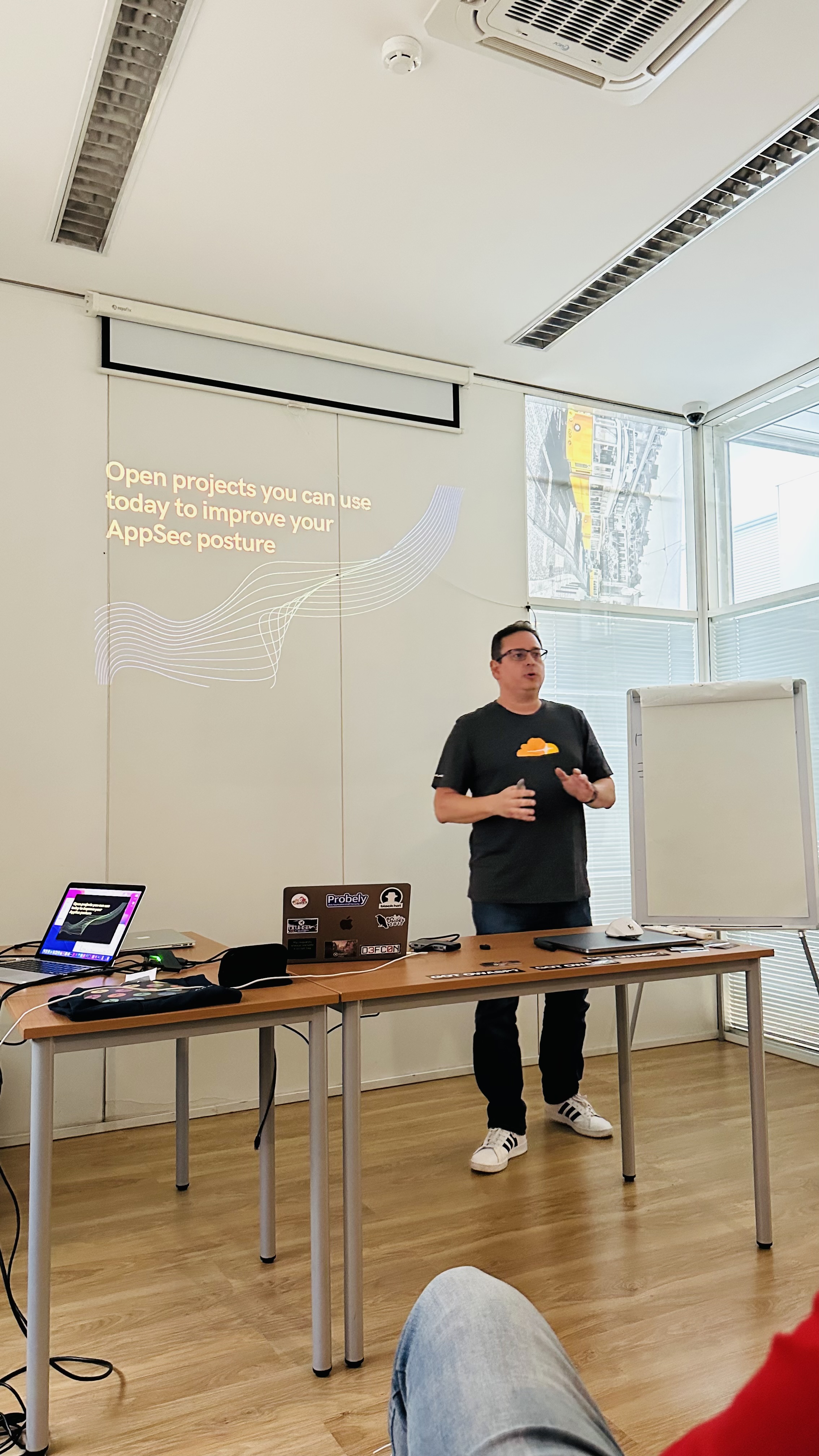 OWASP Lisboa #3 A speaker wearing a black t-shirt presenting a slide with the text "Open projects you can use today to improve your AppSec posture."
