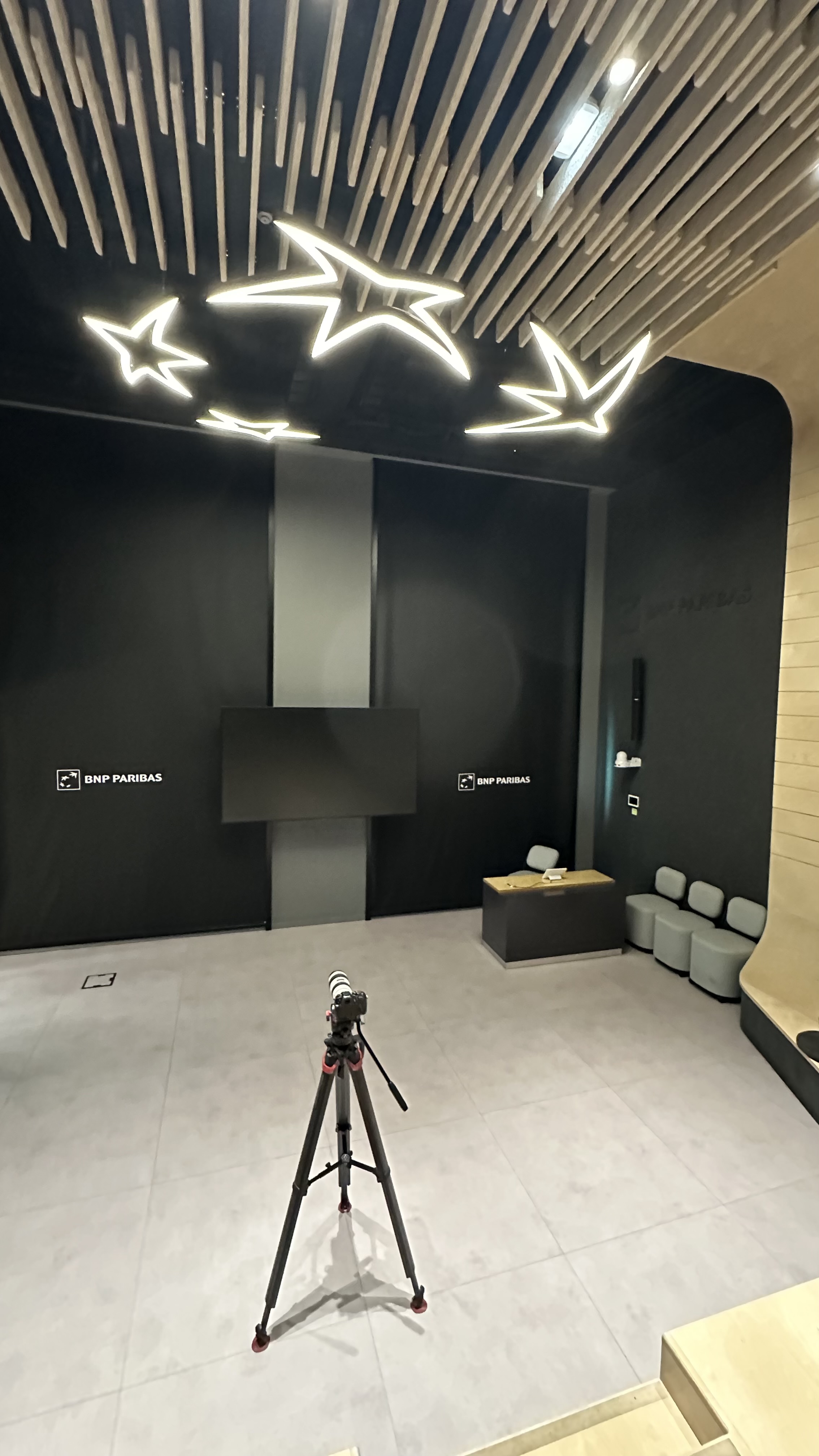 OWASP Lisboa #4 A modern event space with star-shaped ceiling lights and BNP Paribas branding, featuring a camera on a tripod ready to record the session.