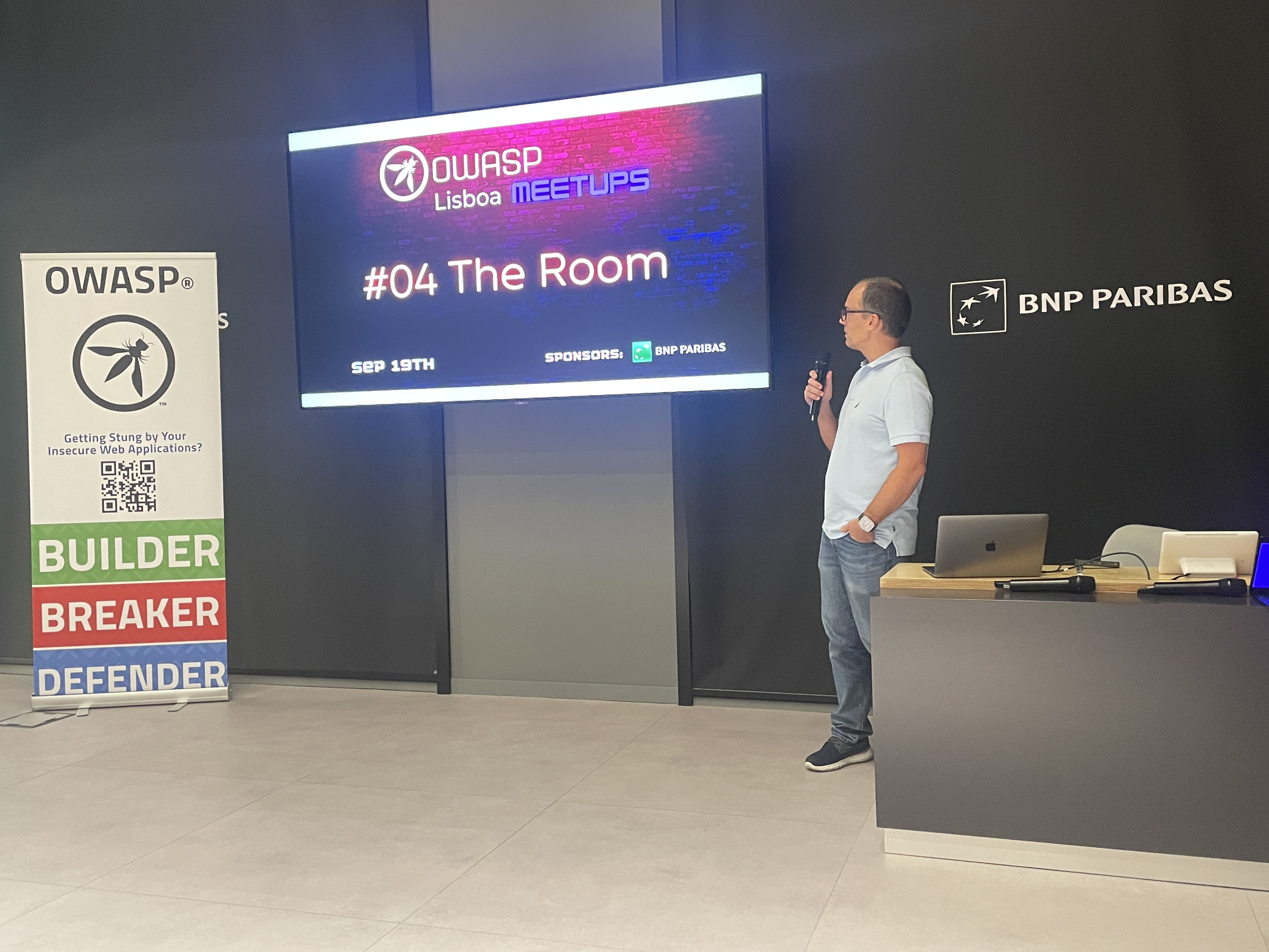 OWASP Lisboa #4 A speaker holding a microphone stands next to the main event screen displaying the "#04 The Room" title slide.