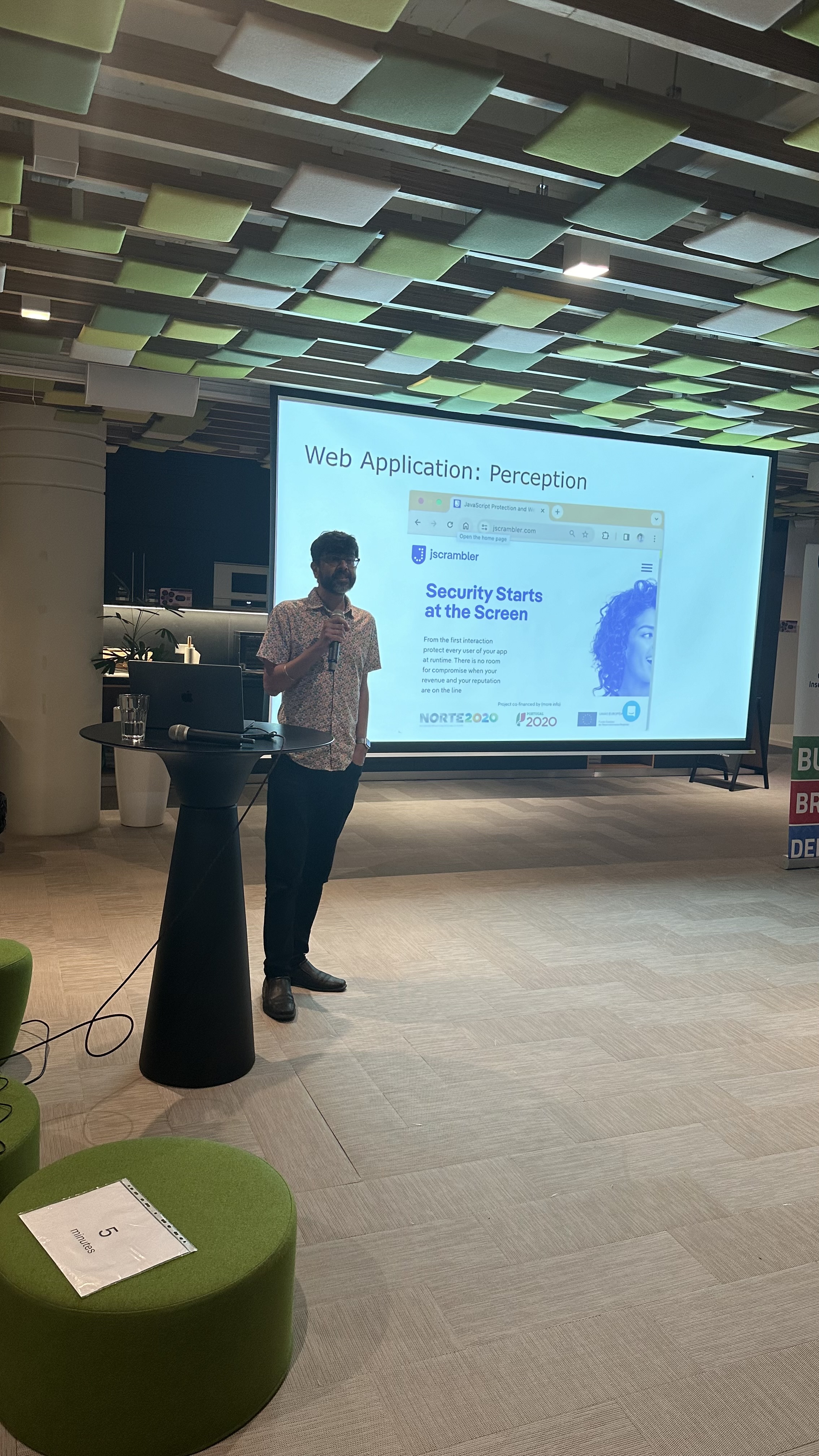 OWASP Lisboa #5 A speaker presenting a slide titled "Web Application: Perception" showing the Jscrambler homepage, standing at a high table.