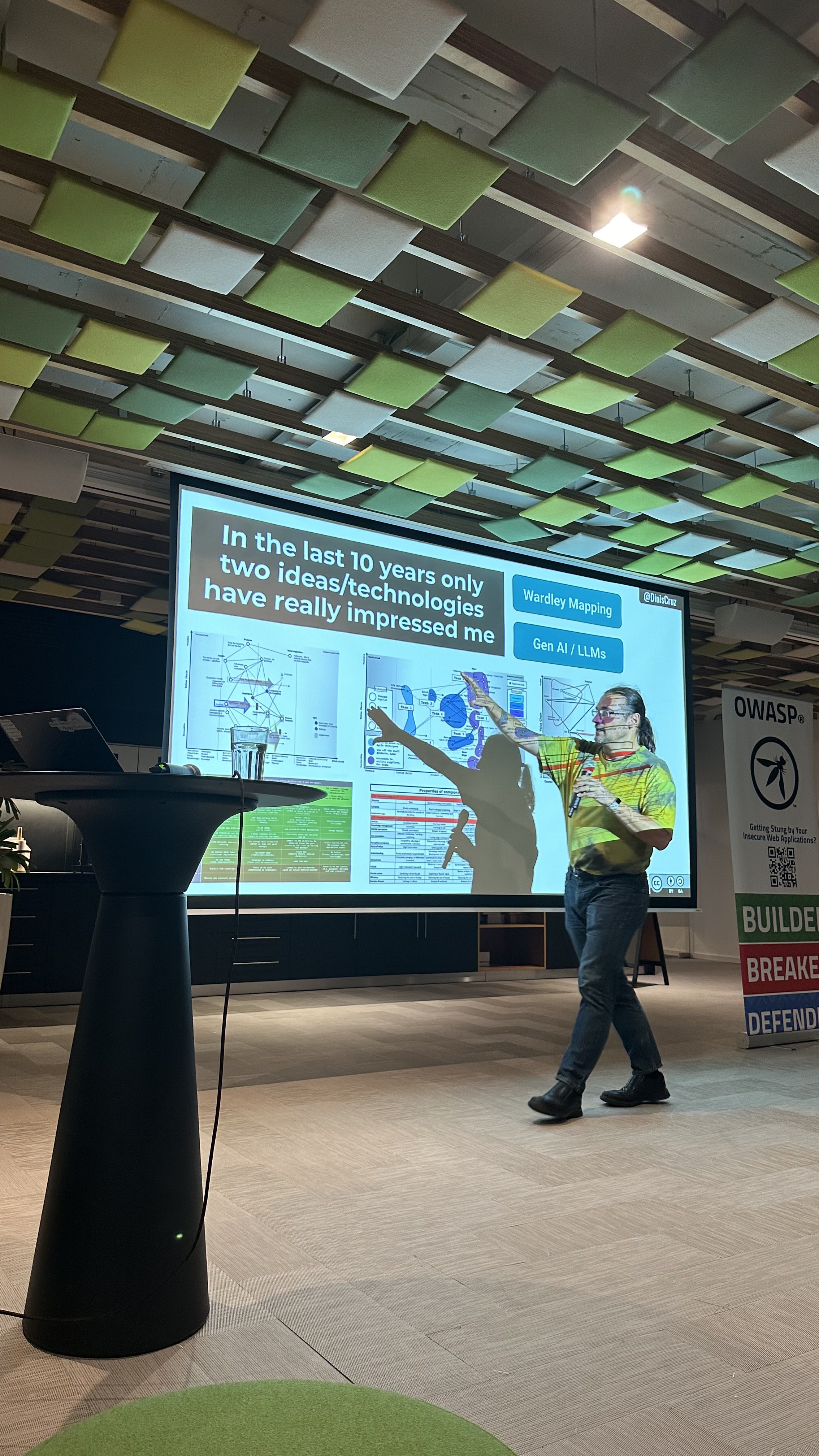 OWASP Lisboa #5 A speaker pointing at a complex diagram on a slide discussing "Wardley Mapping" and "Gen AI / LLMs" as impressive technologies.