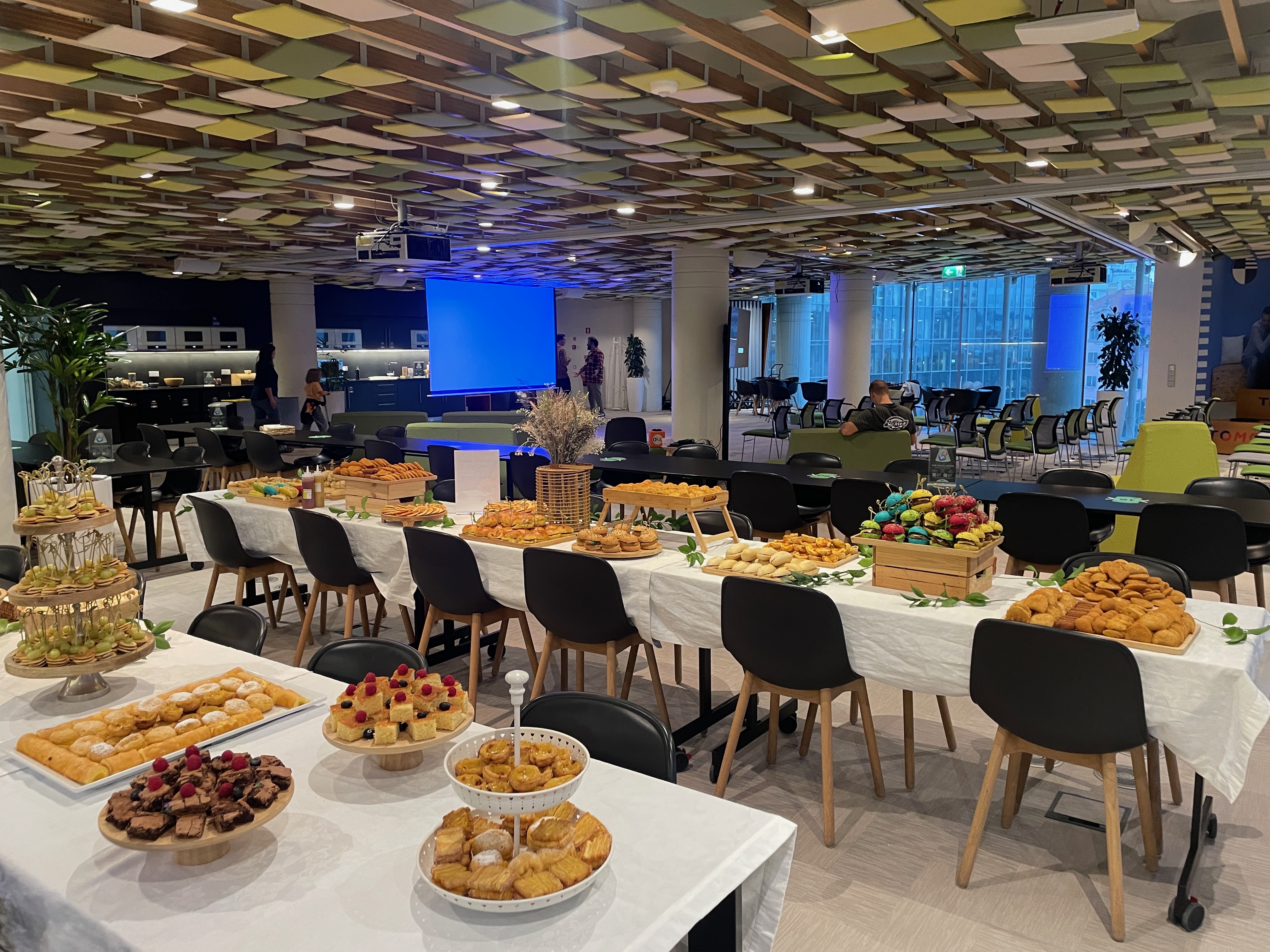 OWASP Lisboa #5 A lavish catering spread on long white tables featuring colorful mini-burgers, pastries, desserts, and fruit in a spacious break area.