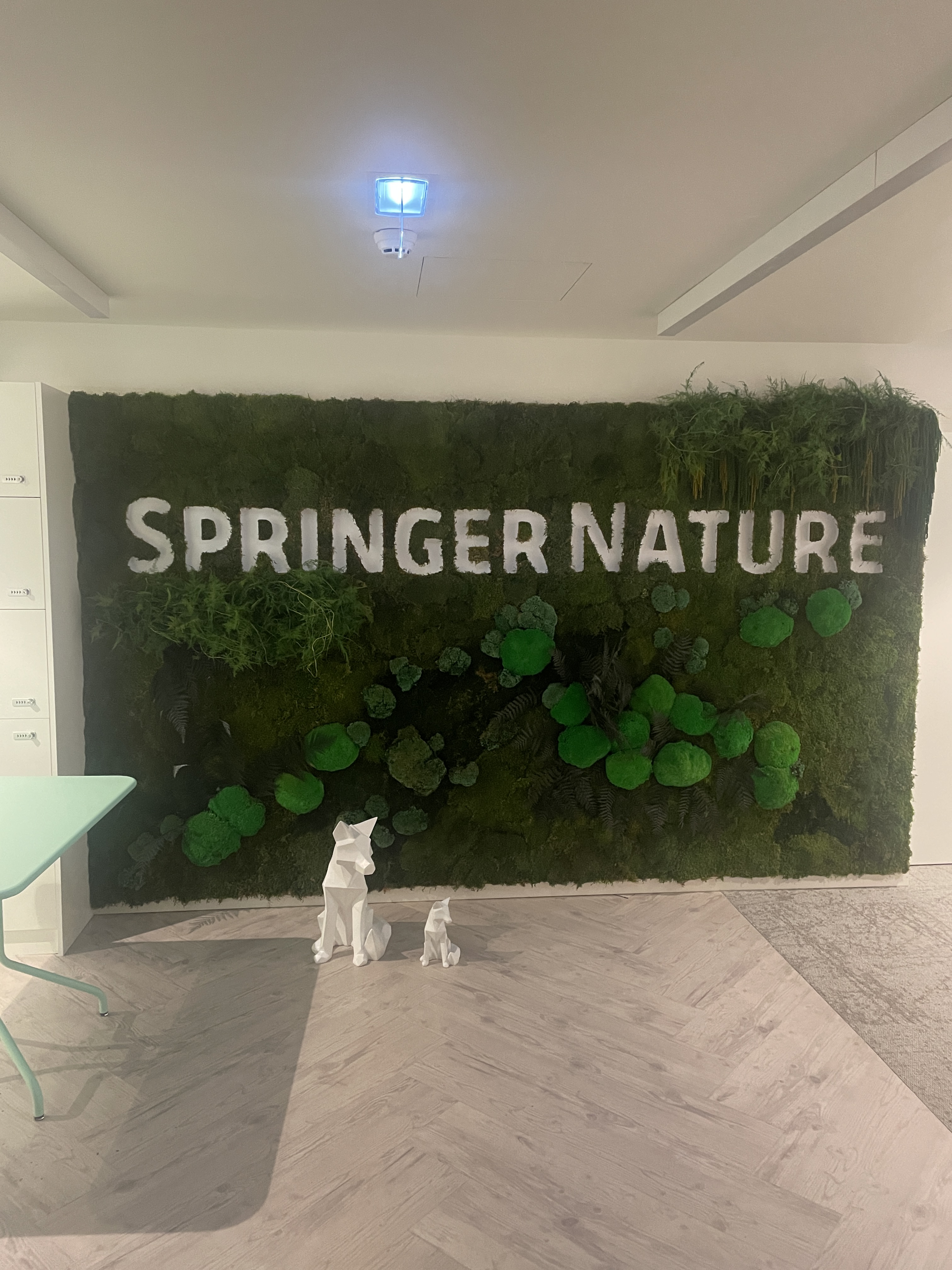 OWASP Lisboa #7 A decorative green moss wall featuring the "Springer Nature" logo in white letters, with two white geometric fox sculptures on the floor in front.