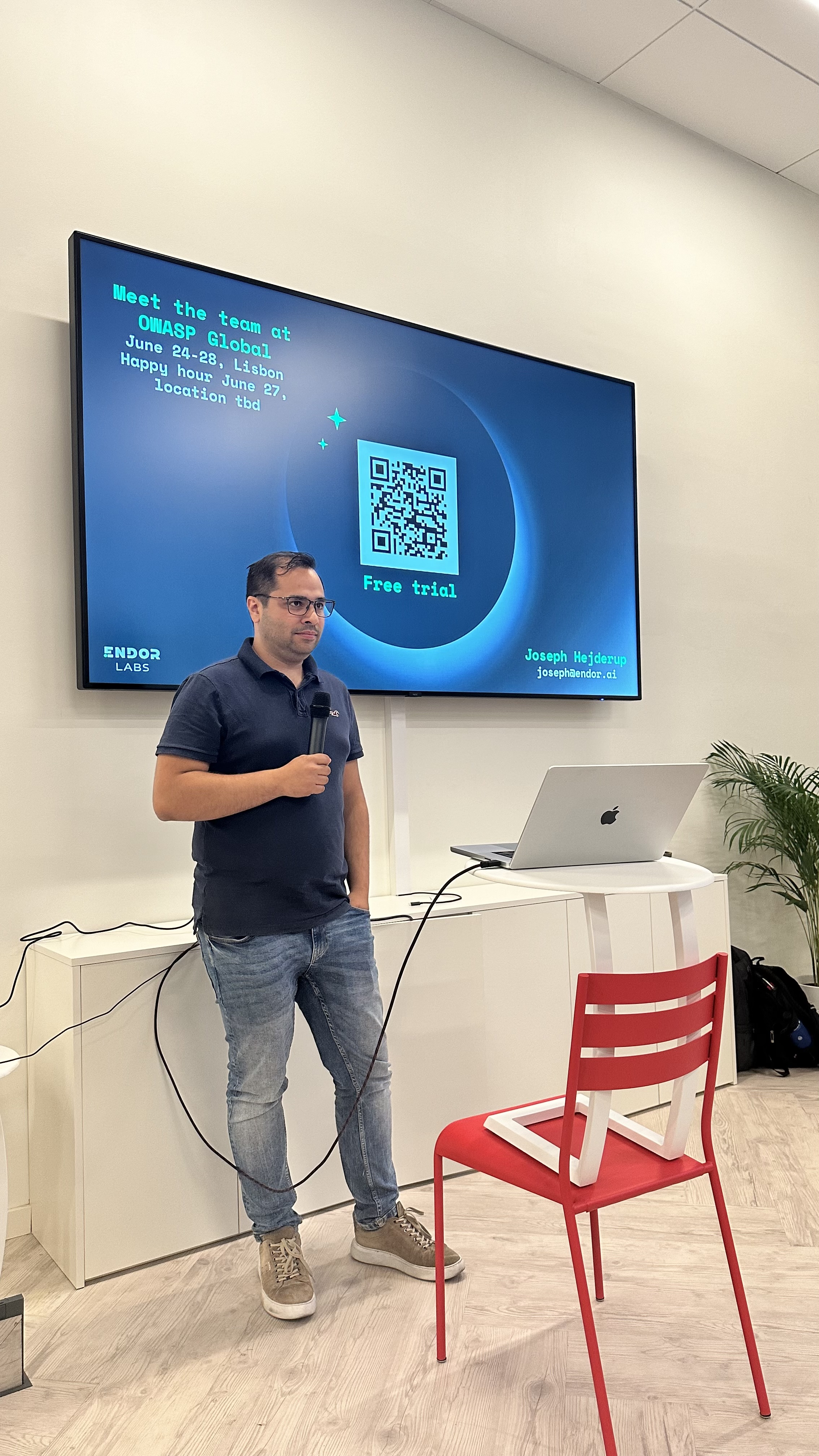 OWASP Lisboa #7 A speaker standing next to a slide inviting attendees to "Meet the team at OWASP Global," displaying a QR code and contact information for Joseph Hejderup from Endor Labs.