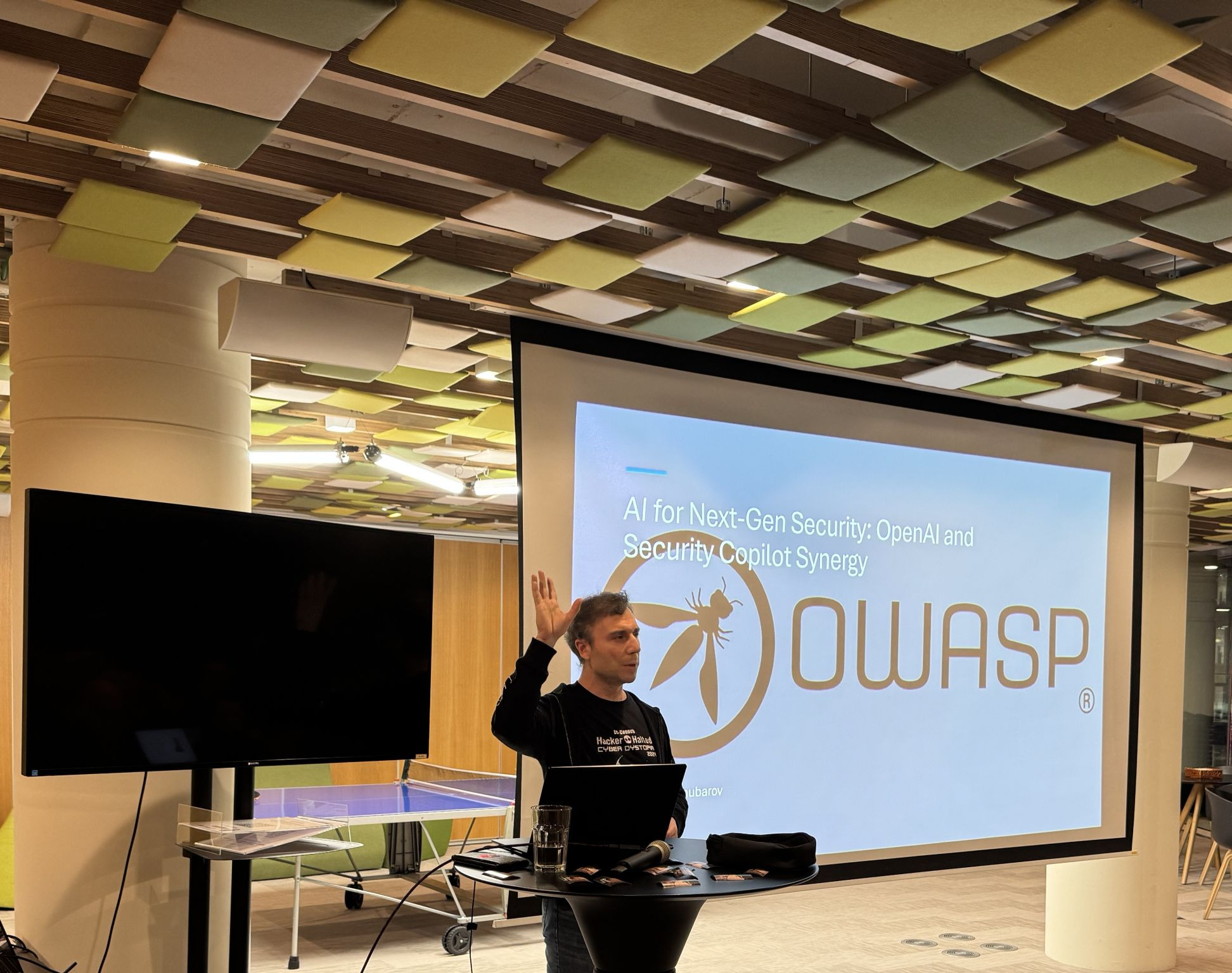 OWASP Lisboa #8 A speaker gesturing with one hand raised while presenting a slide titled "AI for Next-Gen Security: OpenAI and Security Copilot Synergy" featuring a large OWASP logo.