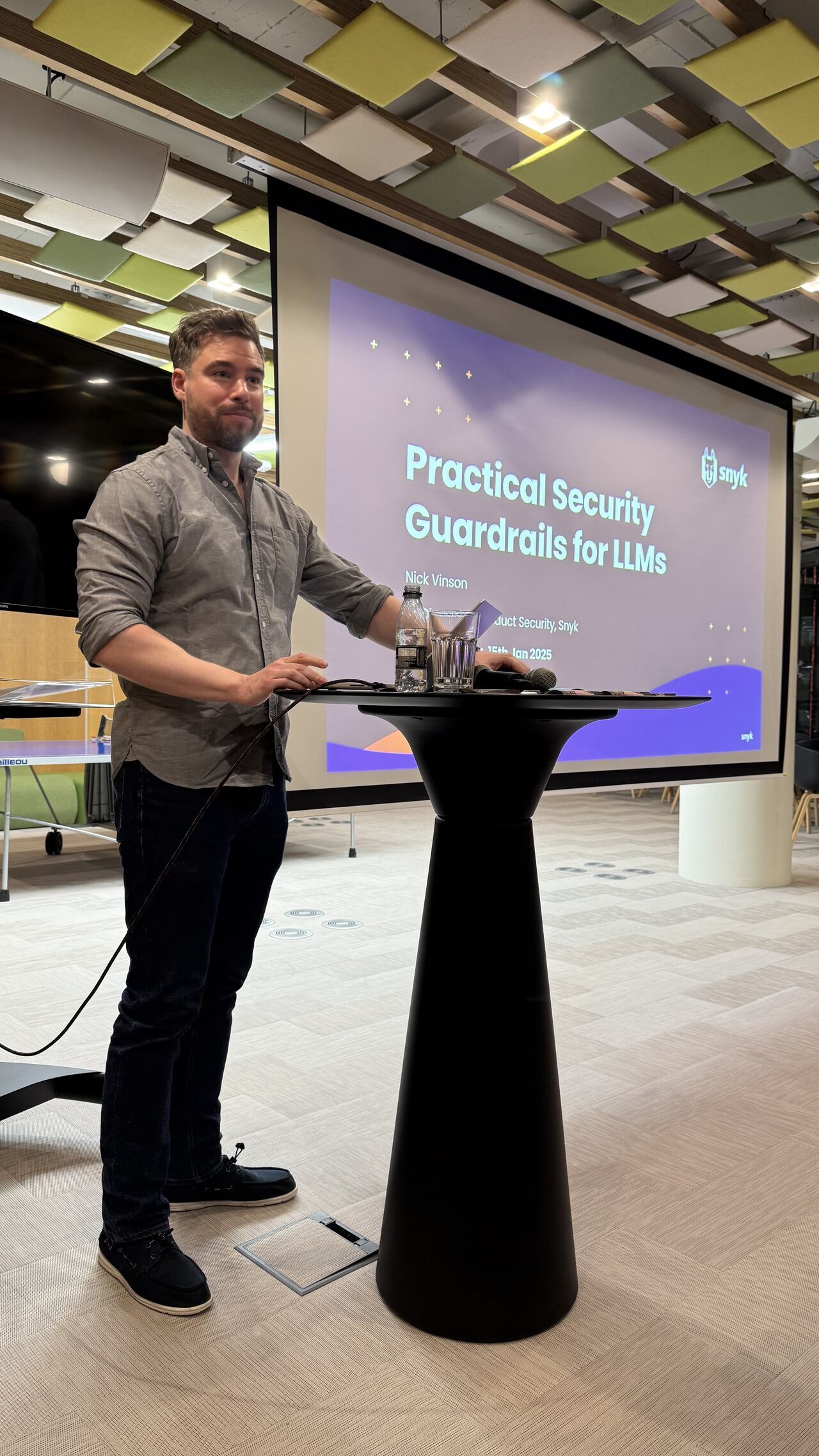 OWASP Lisboa #8 Nick Vinson from Snyk standing at a podium presenting a slide titled "Practical Security Guardrails for LLMs" dated Jan 15th, 2025.