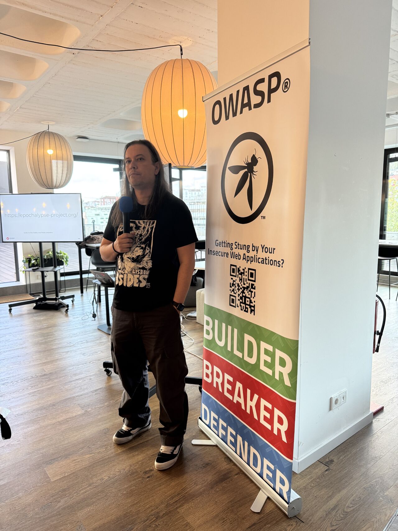 OWASP Lisboa #9 A speaker wearing a black t-shirt stands next to an OWASP banner, displaying a slide with the URL "https://epochalypse-project.org/".