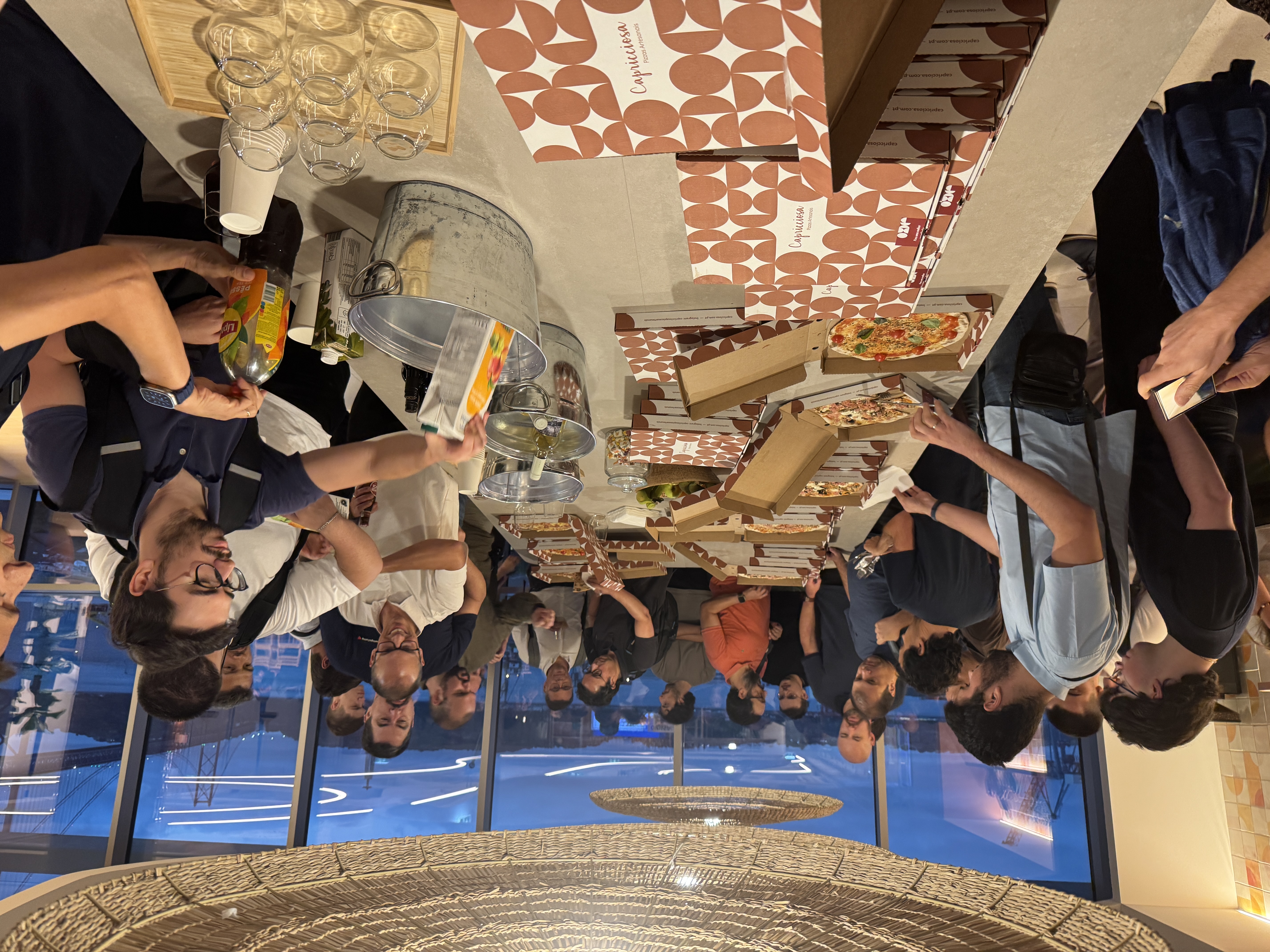 OWASP Lisboa #10 Attendees gathered around a large table filled with open pizza boxes and drinks during the networking session.