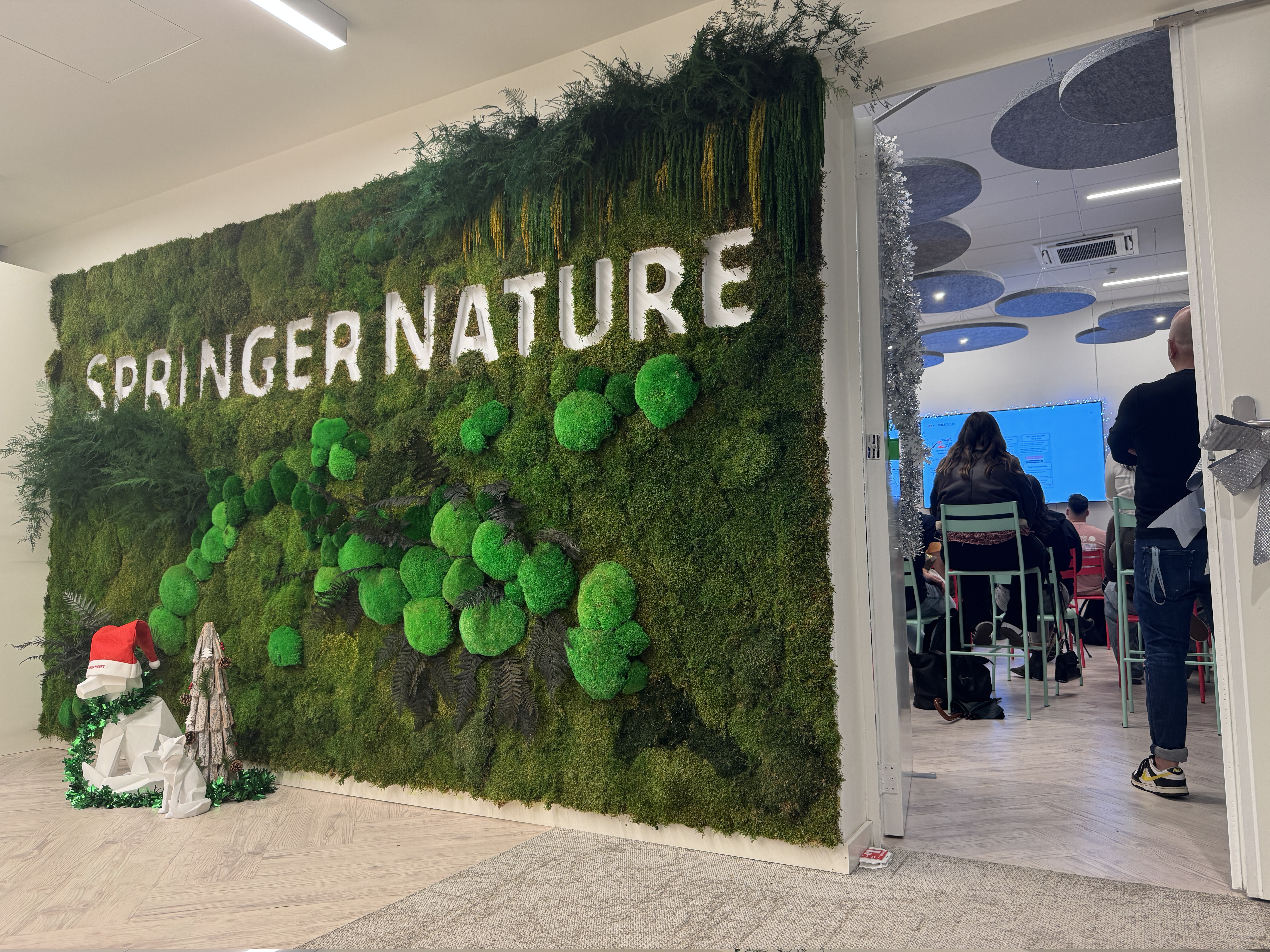 OWASP Lisboa #11 A decorative office wall featuring a moss installation with the "Springer Nature" logo and white fox sculptures, leading into a conference room with attendees.