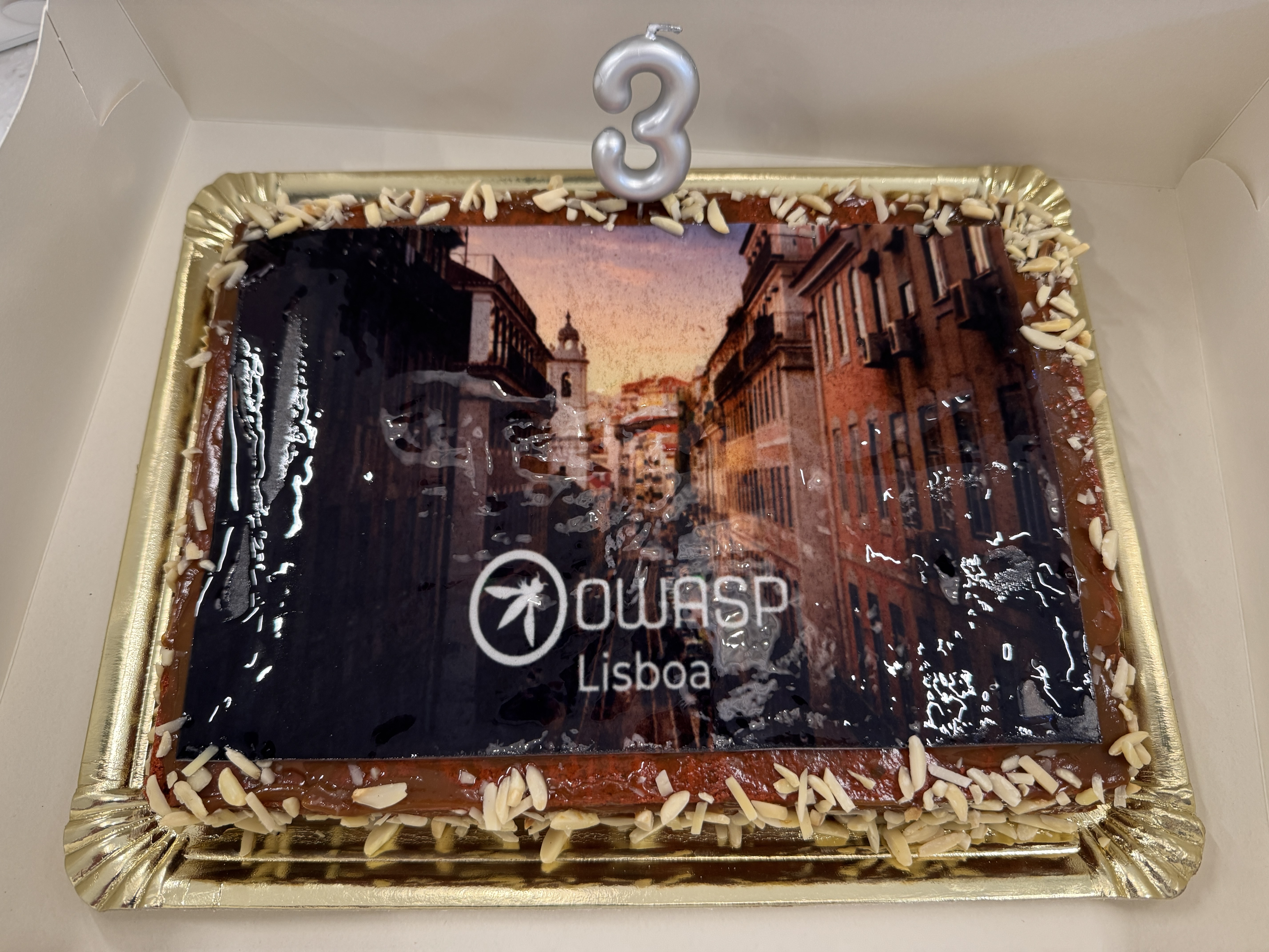 OWASP Lisboa #11 A close-up of the rectangular celebratory cake featuring an edible image of a Lisbon street scene, the OWASP logo, and a silver "3" candle.