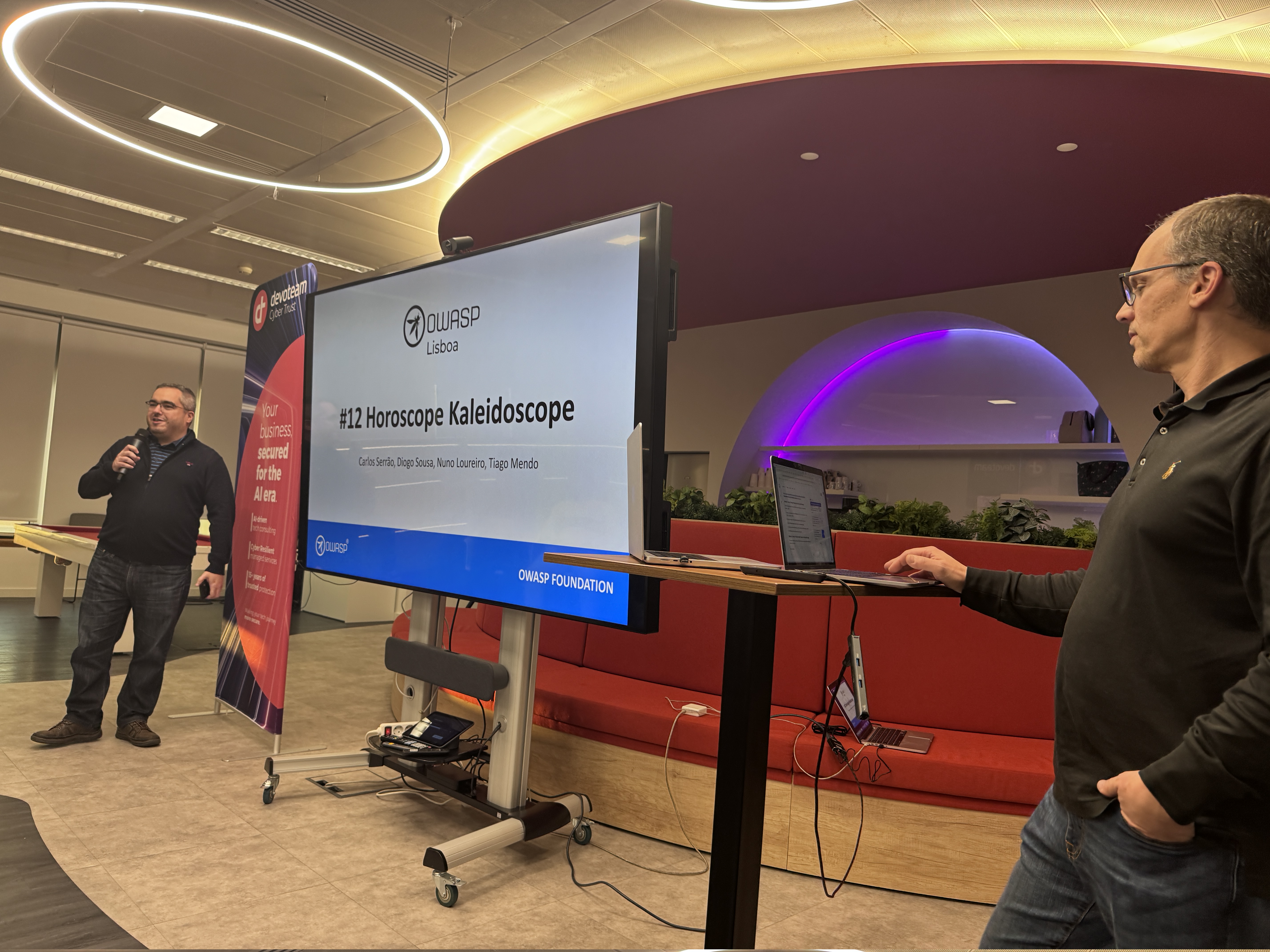 OWASP Lisboa #12 A speaker introduces the OWASP Lisboa #12 meetup titled "Horoscope Kaleidoscope" in a modern presentation space with a large digital screen and circular LED lighting.