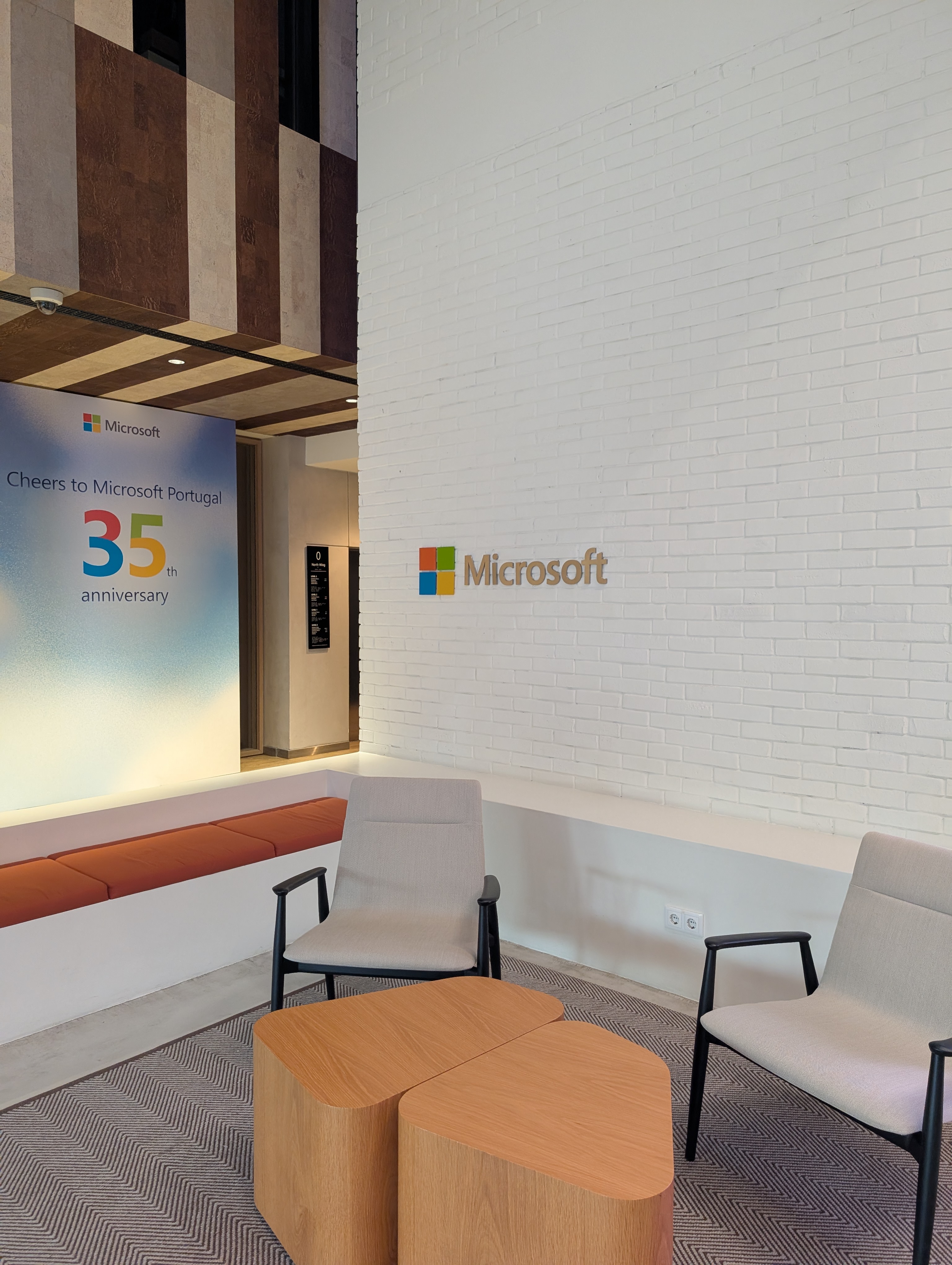 OWASP Lisboa #13 A modern lounge lobby area inside Microsoft Portugal featuring a wall celebrating their 35th anniversary and stylish minimalist armchairs.