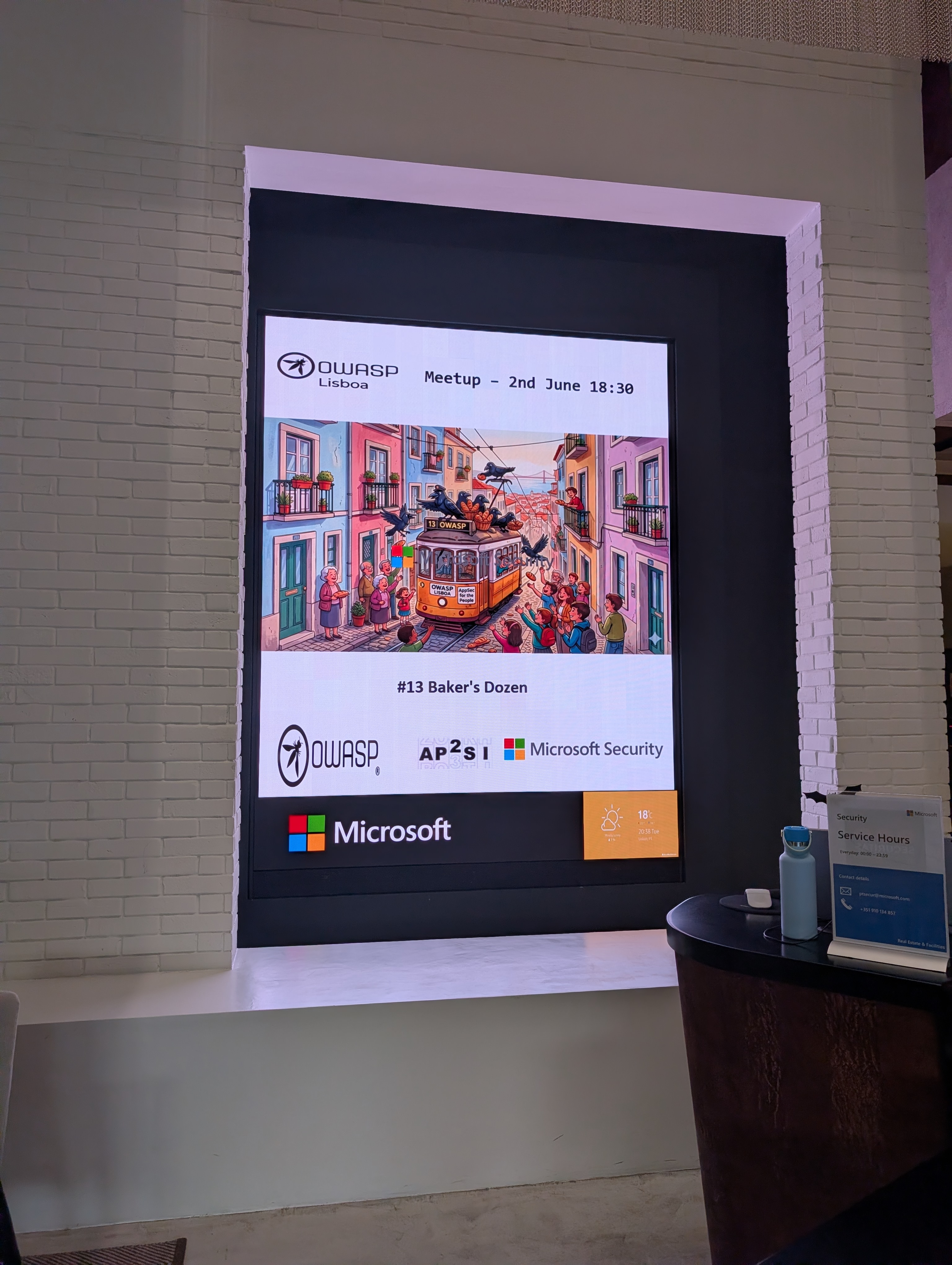 OWASP Lisboa #13 A large wall-mounted digital display welcoming guests to the OWASP Lisboa Meetup on June 2nd, titled "#13 Baker's Dozen," with a custom tram illustration.